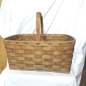 May include: A large, rectangular, woven basket with a wooden handle. The basket is made of natural wood and has a rustic, vintage look.