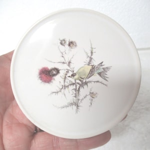 May include: White ceramic coaster with a painted design of a yellow bird perched on a branch with pink and green flowers.