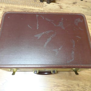 May include: A rectangular suitcase featuring a dark brown textured top lid with visible surface wear and scuff marks. The base of the suitcase is a contrasting light tan color, accented with brass-toned metal latches and a dark brown handle.
