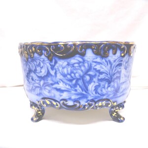 May include: A blue and white porcelain footed bowl with a floral design. The bowl has a gold trim around the rim and on the feet. The floral pattern is a detailed, repeating design. The bowl is rectangular with rounded corners.