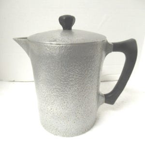 May include: A silver aluminum coffee pot with a black plastic handle and lid. The pot has a textured surface.