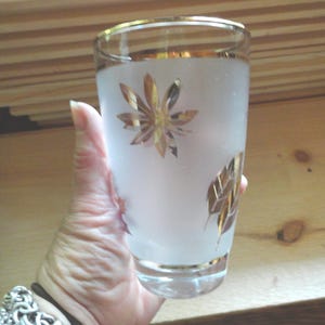 May include: A frosted glass with a gold rim and gold leaf design. The glass has a leaf pattern with a starburst in the center.