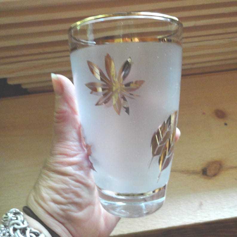 May include: A frosted glass with a gold rim and gold leaf design. The glass has a leaf pattern with a starburst in the center.