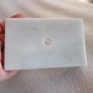 May include: A white marble tile with a round hole in the center.
