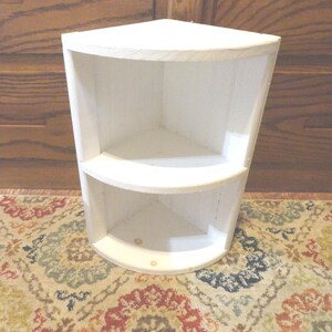 K&ouml;nnte beinhalten: Ein wei&szlig;es Eckregal mit zwei gebogenen Regalen. Das Regal ist aus Holz gefertigt und wei&szlig; lackiert. Die Regale sind so konzipiert, dass sie in eine Ecke passen und den Platz optimal nutzen. Ideal zum Pr&auml;sentieren von Dekorationsartikeln oder zur Aufbewahrung kleiner Gegenst&auml;nde.
