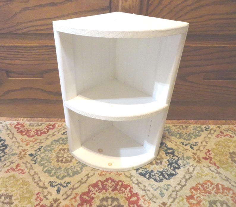 K&ouml;nnte beinhalten: Ein wei&szlig;es Eckregal mit zwei gebogenen Regalen. Das Regal ist aus Holz gefertigt und wei&szlig; lackiert. Die Regale sind so konzipiert, dass sie in eine Ecke passen und den Platz optimal nutzen. Ideal zum Pr&auml;sentieren von Dekorationsartikeln oder zur Aufbewahrung kleiner Gegenst&auml;nde.