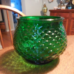 May include: A green glass vase with a textured, scale-like pattern. The vase is round and has a wide opening.