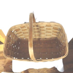 May include: A woven wooden basket with a single handle. The basket is empty and has a rectangular shape.