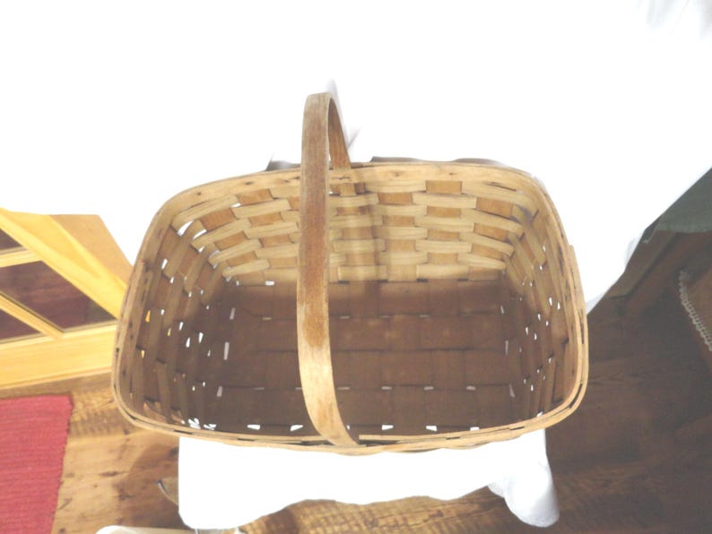 May include: A woven wooden basket with a single handle. The basket is empty and has a rectangular shape.