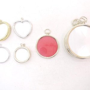 May include: A collection of six metal pendant frames in various shapes and sizes. The set includes two heart-shaped frames in gold and silver, three circular frames in silver, and one large circular frame in silver with a pink insert.