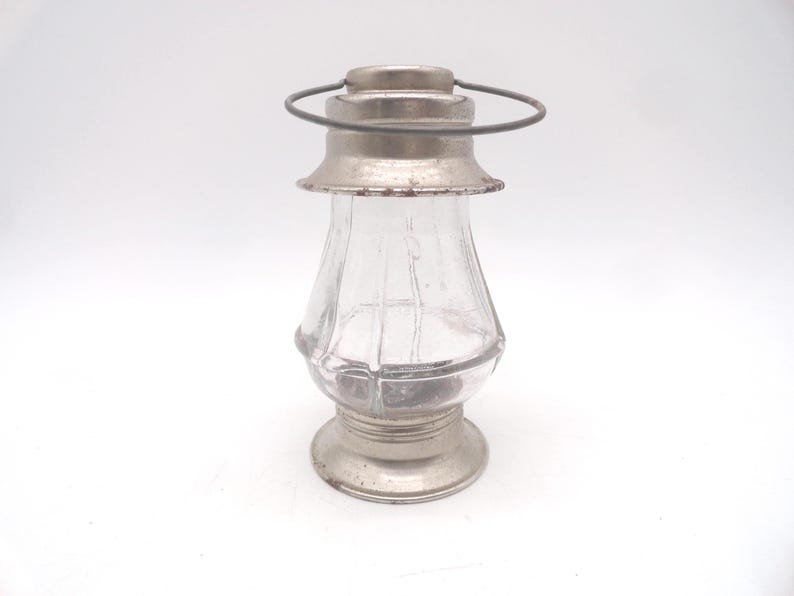 Pu&ograve; includere: Una piccola lanterna in vetro in stile vintage con base, parte superiore e manico in metallo argentato. Il corpo in vetro trasparente ha una forma arrotondata con scanalature verticali. La lanterna &egrave; progettata per contenere una piccola candela o fonte di luce.