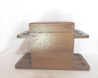 May include: Wooden pipe rack with a hinged lid and multiple slots for storing pipes. The rack is made of dark brown wood with a natural grain pattern.