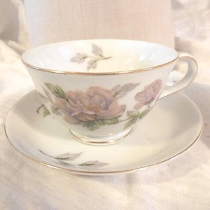 May include: A white teacup and saucer set with a floral design. The cup has a gold rim and the saucer has a gold band around the edge. The flowers are pink and purple with green leaves.