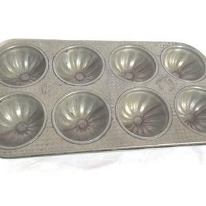 May include: Vintage metal baking pan with eight individual fluted molds. The pan is silver in color and has a slightly worn appearance.