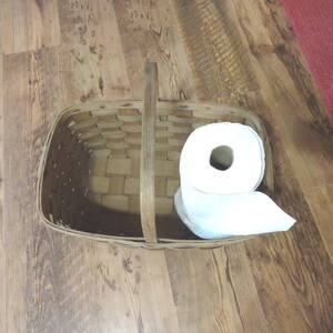 May include: A white roll of paper towels sits inside a brown wicker basket with a wooden handle.