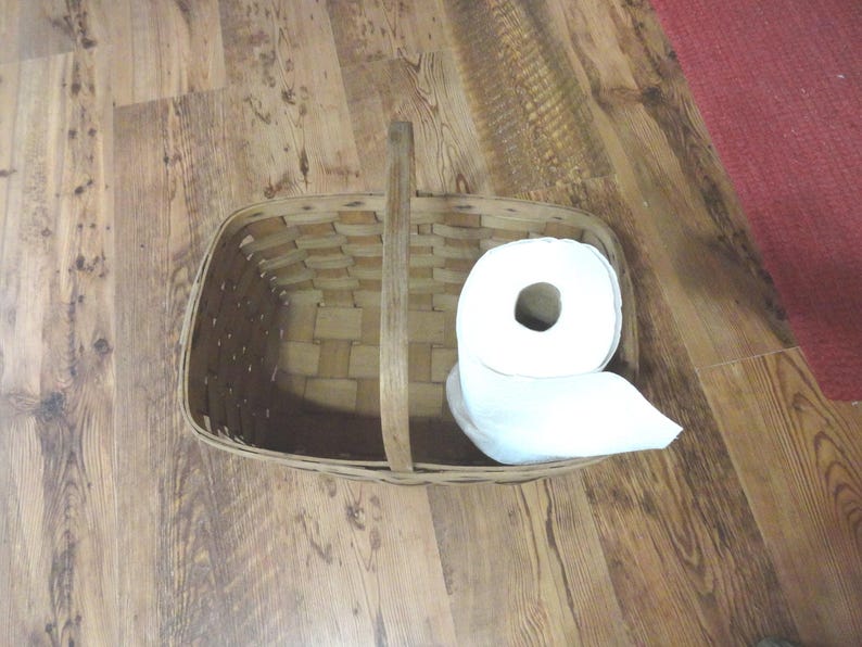 May include: A white roll of paper towels sits inside a brown wicker basket with a wooden handle.