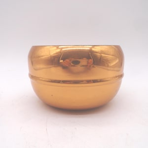 May include: A small, round, gold-colored bowl with a shiny, reflective surface. The bowl has a simple, elegant design, with a slightly wider top and a narrower base. The bowl is likely made of metal and is suitable for decorative purposes.