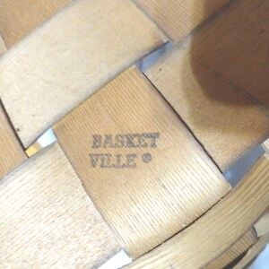 May include: A close-up of a woven wooden basket with the text "Basket Ville" stamped on the bottom.