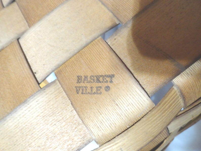 May include: A close-up of a woven wooden basket with the text "Basket Ville" stamped on the bottom.