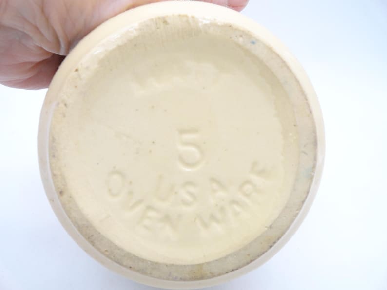May include: Cream-colored ceramic ovenware with the number "5" and the text "U.S.A. OVEN WARE" embossed on the bottom. The piece has a rounded shape and a slightly textured surface.
