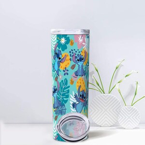 May include: A tall, stainless steel tumbler featuring a repeating pattern of the blue alien character Stitch from Lilo & Stitch. The design is set against a teal background with tropical leaves, flowers, and pineapples. The tumbler includes a silver lid and a clear, circular lid.