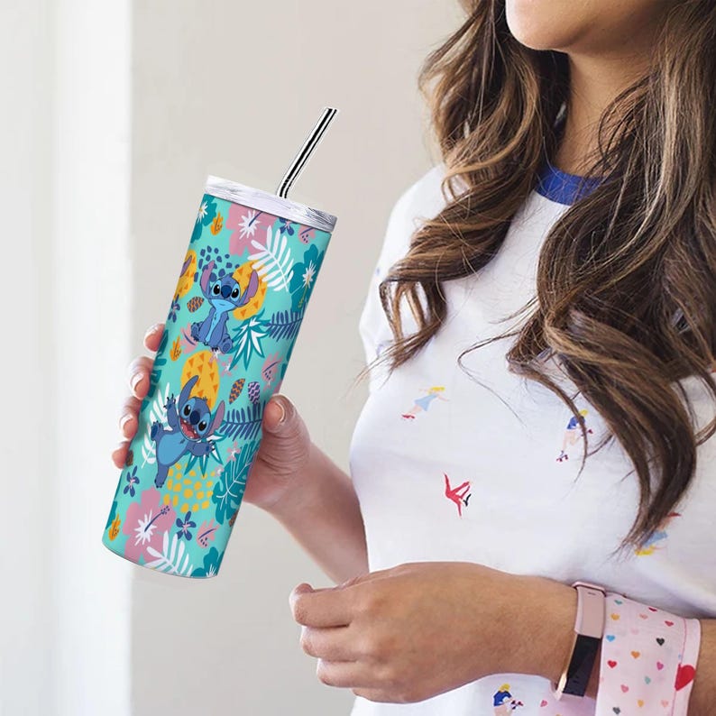 May include: A teal tumbler featuring the character Stitch from Lilo & Stitch, surrounded by a tropical floral pattern. The tumbler has a silver lid and a black and silver striped straw. The design includes blue, yellow, pink, and white elements.