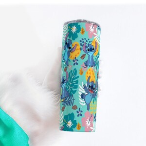 May include: A teal tumbler featuring a repeating pattern of the character Stitch from Lilo & Stitch, pineapples, and tropical flowers. The design includes Stitch in various poses, with a silver lid.