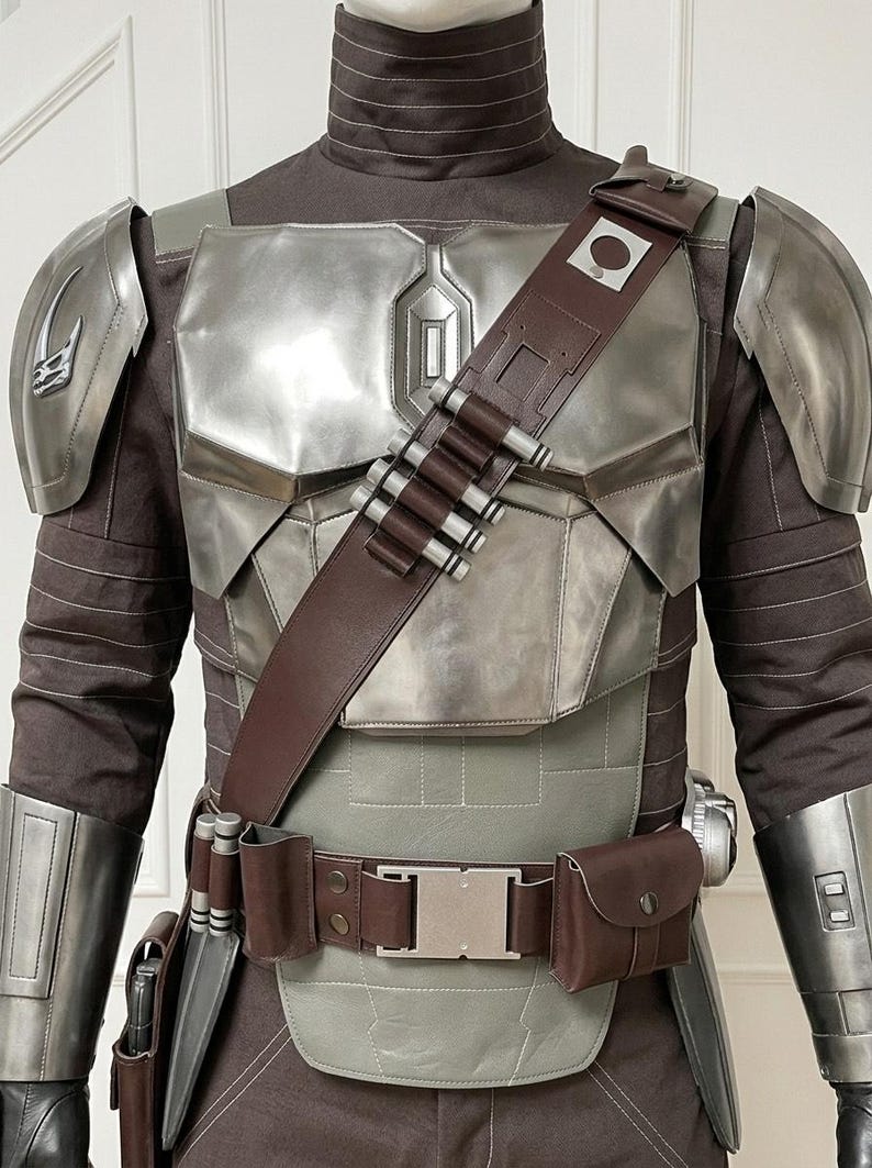 May include: A costume set featuring a dark brown long-sleeved shirt with a high collar, metallic silver chest and shoulder armor, and a brown leather bandolier with silver cylindrical cartridges. A matching brown utility belt includes pouches.