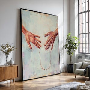 Pode incluir: Obra de arte emoldurada de grandes dimensões com duas mãos estendidas uma para a outra, ligadas por um fio vermelho. A pintura tem uma paleta de cores pastel suaves com um fundo azul claro e creme. A obra de arte é exibida numa sala de estar moderna.