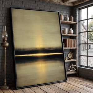 May include: A large, framed abstract painting with a black border. The artwork features a gradient of gold and black hues, with a horizontal band of bright yellow light. The painting is leaning against a brick wall in a room with a wooden floor.