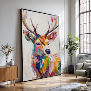 Puede incluir: Gran arte en lienzo enmarcado que presenta una pintura abstracta colorida de un ciervo. La obra de arte utiliza una paleta de colores vibrantes, incluyendo rosa, azul, amarillo y verde, aplicada con pinceladas visibles. Las astas del ciervo son marrones y el fondo es blanco.