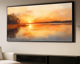 Puede incluir: Pintura de paisaje enmarcada que representa una puesta de sol sobre un lago tranquilo. El cielo es una mezcla de tonos naranja y amarillo, reflejándose en la superficie del agua. Árboles oscuros bordean la orilla distante, sobre un mueble negro.