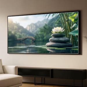 May include: A framed wall art print depicting a serene zen garden scene. The image features a stack of smooth, gray stones topped with a white lotus flower, set against a backdrop of a tranquil pond, bridge, and lush greenery.