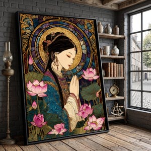 Könnte beinhalten: Gerahmtes Kunstwerk mit einer Frau in traditioneller Kleidung, die die Hände zum Gebet gefaltet hat. Das Bild hat einen Buntglasstil mit goldenem Heiligenschein, Lotusblumen und einem blau-goldenen Farbschema. Das Kunstwerk wird in einem Raum mit Backsteinmauer und Holzboden ausgestellt.