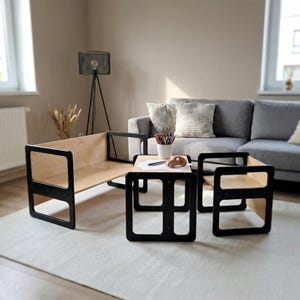 May include: A modern children's furniture set featuring a low, open-sided bench and two square tables with black frames and natural wood surfaces. A small wooden car and art supplies sit on one table. The set is on a light-colored rug.