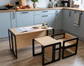 May include: A light wood children's table and chair set with black frames. The table has a coloring book and colored pencils on top. The chair is a small, open-sided box design. The set is in a kitchen setting.