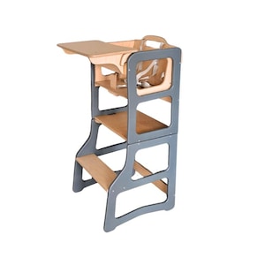 Può includere: Una torre di apprendimento in legno con struttura grigia e dettagli in legno naturale. Presenta un tavolino, un sedile con cinture di sicurezza e più piattaforme per arrampicarsi. Progettata per bambini piccoli.