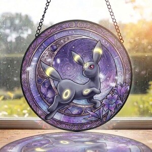 May include: A circular stained glass suncatcher featuring a dark gray creature with yellow ring markings, set against a purple celestial background with a crescent moon, stars, and purple flowers, suspended by a black metal chain for display.