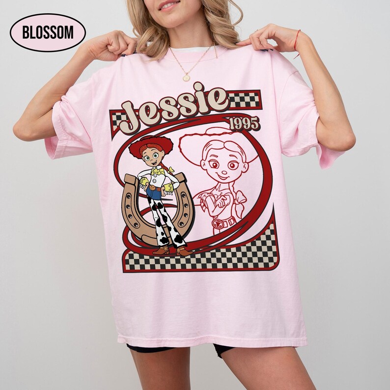 Peut inclure: T-shirt rose clair avec un motif de Jessie, personnage de Toy Story. Le design comprend le nom "Jessie", l'ann&eacute;e "1995" et une image de Jessie avec un fer &agrave; cheval. Le t-shirt est ample.
