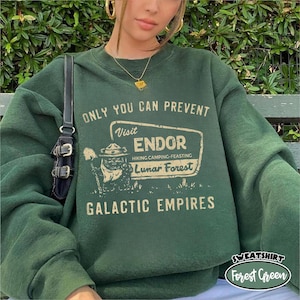May include: Forest green sweatshirt featuring the text "ONLY YOU CAN PREVENT" and "Visit Endor Hiking Camping-Feasting Lunar Forest Galactic Empires". The sweatshirt has a graphic of a character in a park ranger hat.