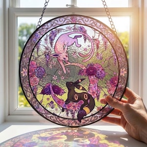 May include: A circular stained glass suncatcher featuring a pink Espeon and a black Umbreon surrounded by purple and pink floral motifs. The design is enclosed in a decorative border and hangs from a metal chain, casting colorful light patterns.