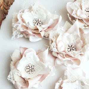 small fabric flowers made with bits of burlap, cotton, and lace. the center is accented by rhinestone small buttons. blush and ivory colors