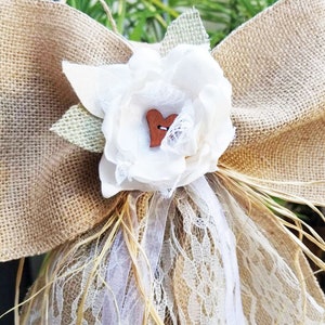 May include: A burlap and lace wedding or baptism decoration with a white fabric flower and a small wooden heart.