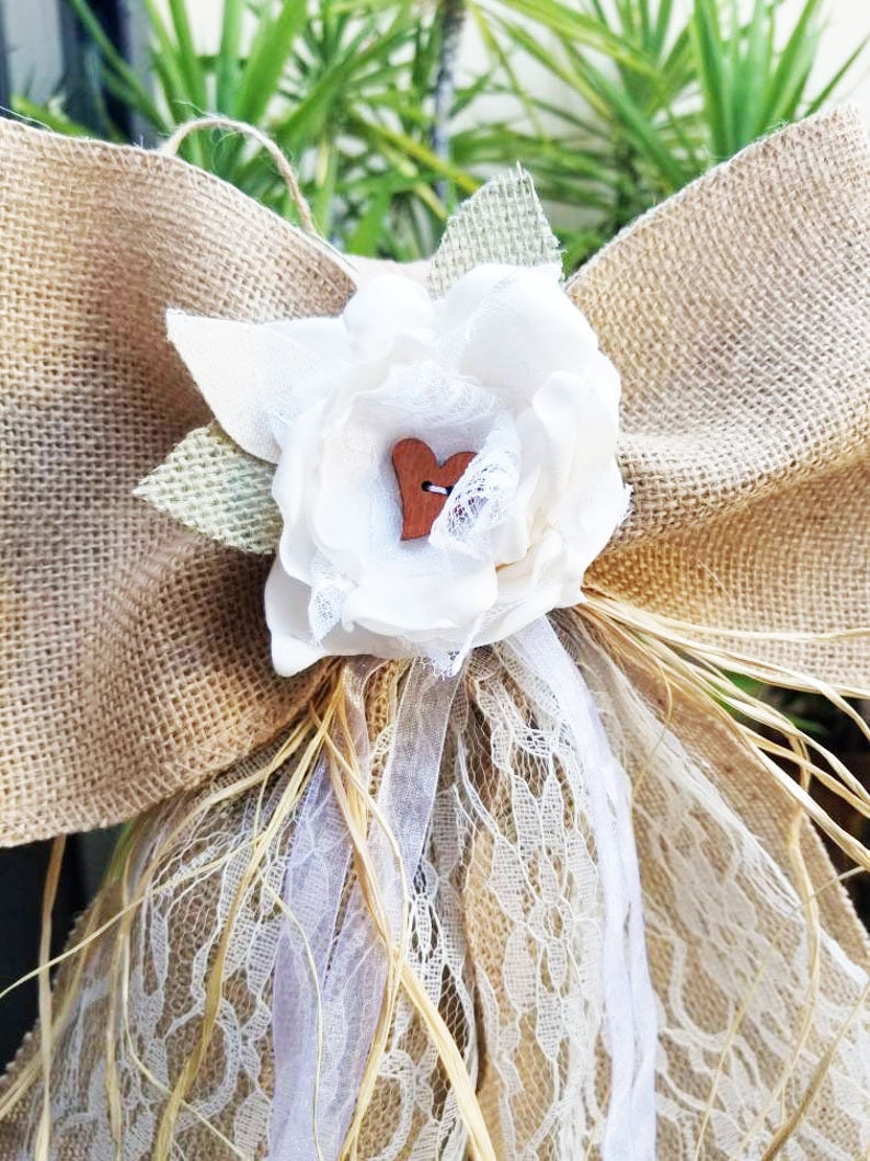 May include: A burlap and lace wedding or baptism decoration with a white fabric flower and a small wooden heart.