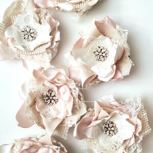 small fabric flowers made with bits of burlap, cotton, and lace. the center is accented by rhinestone small buttons. blush and ivory colors