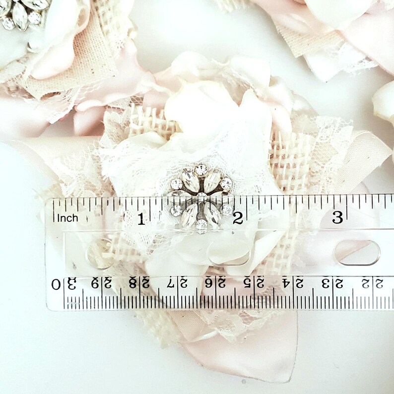small fabric flowers made with bits of burlap, cotton, and lace. the center is accented by rhinestone small buttons. blush and ivory colors