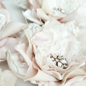 small fabric flowers made with bits of burlap, cotton, and lace. the center is accented by rhinestone small buttons. blush and ivory colors