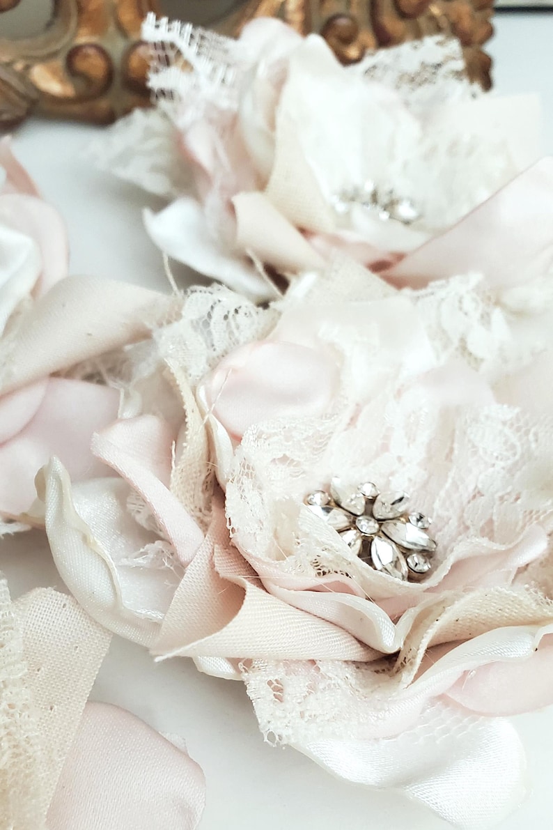 small fabric flowers made with bits of burlap, cotton, and lace. the center is accented by rhinestone small buttons. blush and ivory colors