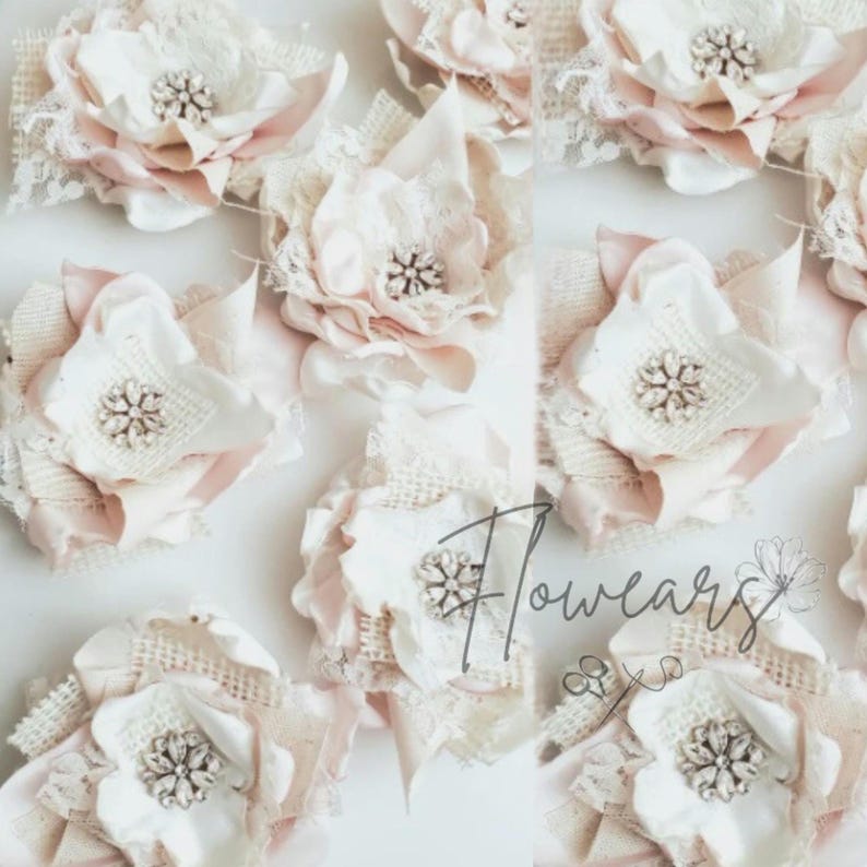 small fabric flowers made with bits of burlap, cotton, and lace. the center is accented by rhinestone small buttons. blush and ivory colors