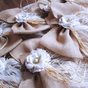 May include: A collection of burlap bows with white lace and a white flower accent. The bows are tied with twine and have wheat stalks attached.